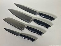 Top view of four Lagostina kitchen knives laid out side by side showing blades and black handles.