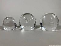 Front view of three clear glass paperweights with air bubbles inside, arranged from smallest to largest.