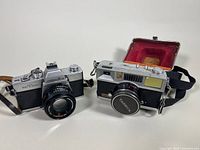 Photo showing Minolta SRT200 camera with attached 50mm lens and Yashica Flash-O-Set camera with case.