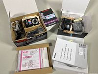 Both Nikon Coolpix S4100 and Pentax Optio S12 digital cameras in original boxes with accessories and manuals.