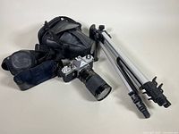 Pentax camera with Vivitar lens, carrying bag, and tripod displayed from side angle on white background.