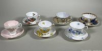Photo of all six teacups and saucers arranged in two rows showing variety of floral designs and brands