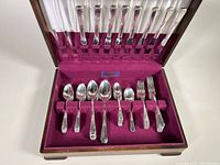 Wood chest containing silver plated cutlery pieces including knives stored vertically in the lid and spoons and forks laid in slots in the base.