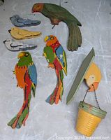 Seven colorful hand painted folk art wooden birds arranged on gray surface showing varying sizes and shapes, largest about 10 inches