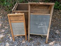 Two old wooden washboards standing outdoors on gravel. Larger labeled 'Economy' by Mahwah Woodenward Co., smaller labeled by Columbus Washboard Co.