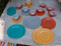 Top view of entire child's tea set including four matching cups, four saucers, and four plates in Fiesta colors of turquoise, gray, orange, and yellow, arranged on a table.