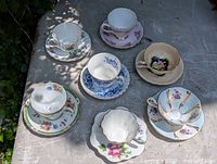 Top-down photo showing all 7 antique tea cups and matching saucers with varied floral patterns and color schemes.