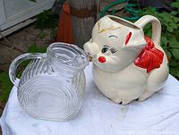 View of the clear textured glass water jug showing circular swirl pattern and handle alongside the ceramic pig pitcher.
