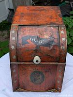 Front view showing roll-top door with 'GLUE' label and white knob, worn orange paint, and white stars along edges.
