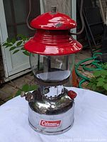 Front and side view of the Coleman lantern showing the red top, glass globe, and chrome base with Coleman logo.