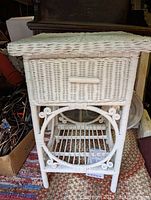 Front view photo of white wicker side table showing drawer detail and lower shelf with circular wicker decoration on legs