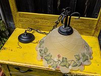 Side view of the hanging floral glass lamp showing hand-painted green leaves and pink flowers decoration, wired chain, and black metal fixture