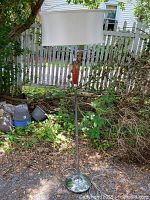 Full view of the standing lamp showing chrome pole with wood accent and oval white fabric shade.