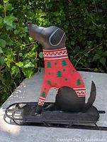 Front-left-side view of metal Christmas dog figurine on sled showing the dog in red sweater with Christmas tree patterns and sled platform