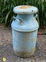 Full view of blue metal milk can with lid, rust spots visible