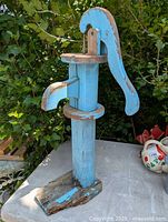 Full view of blue painted wooden hand pump garden art with rustic wear and visible base damage.