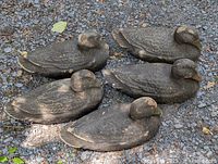 Five vintage paper mache duck decoys grouped on gravel surface showing wear and painted feather detail.