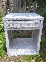 Front angle view of the white wicker side table showing drawer detail and bottom shelf
