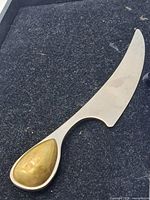 Full view of stainless cheese knife with curved blade and teardrop inlay handle