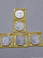 Five Morgan silver dollars in yellow cardboard flips with handwritten dates visible