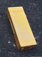 Front and top view of gold-tone textured Dunhill lighter on fabric background
