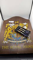 Wooden dartboard cabinet with royal crest design and three feather-weighted darts in black case on top.
