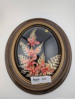 Front view of vintage Hawaiian real floral arrangement with convex dome oval wooden frame, showing pink real flowers and gold-dipped fern leaves with small gold butterfly on black background.