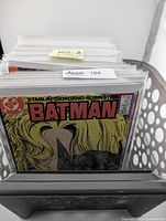Stack of Batman comic books in protective sleeves with visible DC logo and Batman title. The first comic in the stack is Batman issue #421 with the cover featuring a close-up illustration of a woman's face with long blonde hair.