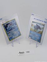 Two Suicune Pokémon cards upright in clear protective sleeves on plastic stands, showing card details and pricing.