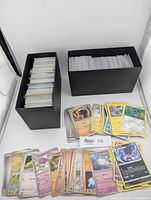 Two black rectangular boxes filled with sleeved English Pokemon trading cards, card fronts showing various Pokemon including Litwick and Hoothoot.