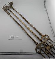 Three brass toasting forks laid out flat showing full length and tops with decorative handles. Two horse head and one ship design are clearly visible. The forks are long with three prongs and cut-out shape in base of fork head.