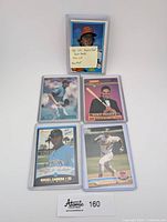 Five baseball cards in protective sleeves arranged flat on white background showing different players and card designs.