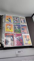 Page of baseball cards in clear plastic sleeves inside binder, showing front images of nine cards with players in baseball uniforms.