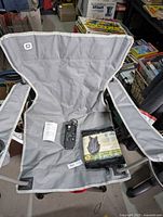 Grey Outbound brand camping chair with armrests and fabric seat shown fully open with flashlight and poncho on the seat.
