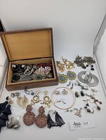 Lot of various handcrafted earrings arranged loosely with a wooden box containing additional earrings