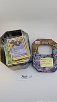 Photo showing metal tin filled with Pokemon cards and separate lid with note indicating 123 cards included with over $200 value, including popular Pokemon, holos, and reverses in NM to VLP condition.