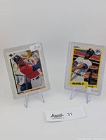 Both cards displayed upright in clear sleeves on stands with price tags visible