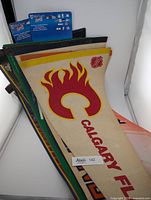 Stack of multiple NHL hockey team pennants visible with Calgary Flames vintage pennant on top in red and yellow colors
