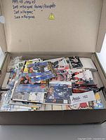 Open box filled with a large quantity of assorted hockey cards, with handwritten notes on the lid indicating years and sets included like 1995 UD, 1996 UD, 2005 In The Game Heroes/Prospects, 2001 and 2006 In The Game.
