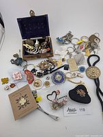 Lot of various vintage pins and keychains assorted on a flat surface next to a small box