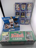 Photo showing sealed box of 1991 Topps Football cards complete set with Barry Sanders image and unopened Panini 1992 football card box.