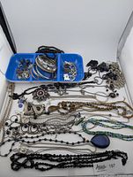 Wide view of assorted silver, black, and earthy toned jewelry including earrings, bracelets, necklaces, and rings arranged on a white background