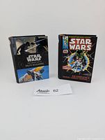 Photo of the two mini books side by side on a white background with a lot number card showing the lot number 62.