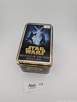 Closed metal tin box featuring Star Wars Revenge of the Sith artwork on lid with two lightsabers crossed and characters fighting.