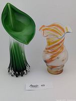 Front view of two art glass vases: tall green and white with leaf shape, and shorter multi-coloured ruffle vase