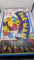 Top view of Pac-Man board game box showing colorful Pac-Man ghost characters and maze artwork with Milton Bradley branding.