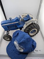 Vintage diecast Ford 8000 tractor model with paint wear and blue Ford hat on front.