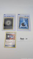 Three Pokémon cards laid out on white background with label Atomic 24: WoTC Rainbow Energy promo, HeartGold SoulSilver Water Energy, and reversed holo Pokémon Catcher.