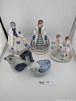 Five porcelain figurines: two Derby-style Victorian ladies, a porcelain couple, a rooster, and a duck with blue and gold accents.