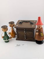 Three wooden Erzgebirge items: two candle holders shaped as figures, a Räuchermann smoker figure, and a wooden coaster holder box